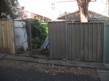 Colorbond posts and one panel in place with an open bay beside a timber paling neighbour fence