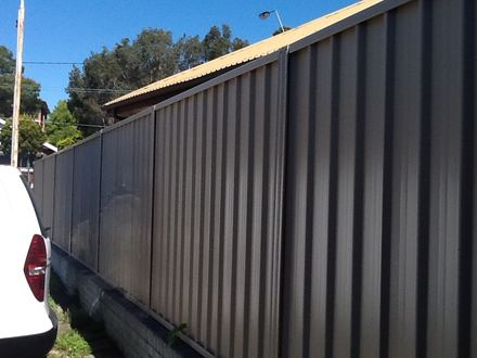 Dark Colorbond privacy fence on the other side of the same boundary, on a concrete plinth