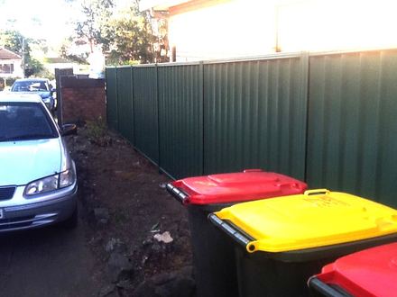 New green Colorbond privacy fence along the same driveway beside the bins