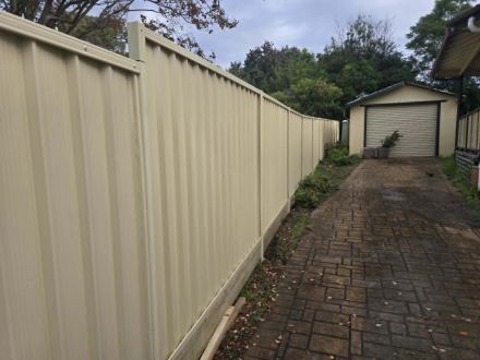 Finished cream Colorbond privacy fence beside the paved drive to the garage