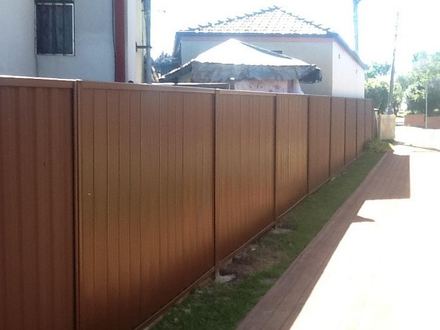 New brown Colorbond privacy fence running beside a paved driveway