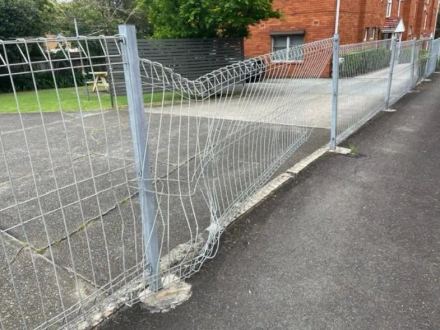 Crushed galvanised mesh panel sagging beside an apartment driveway