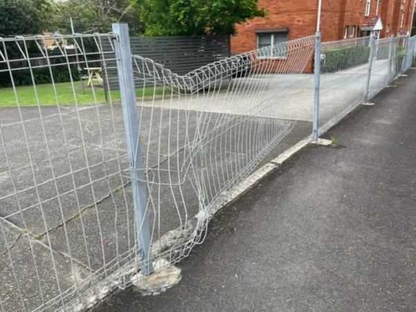 Crushed galvanised mesh panel sagging beside an apartment driveway