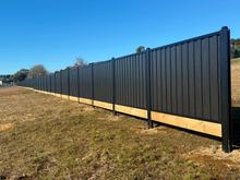 Long run of Black Ash woodgrain steel fencing on a timber plinth in open ground