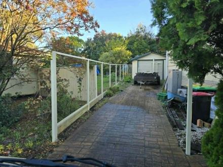 Cream Colorbond posts and rails set along the paved drive toward the garage