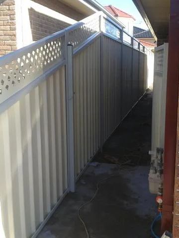 Cream Colorbond privacy fence with a lattice topper running beside a brick house
