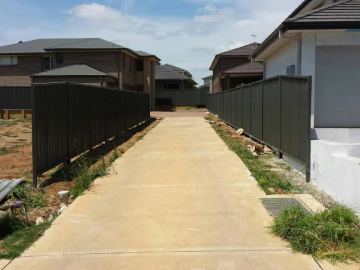 Dark Colorbond privacy fence running the length of a concrete driveway between houses