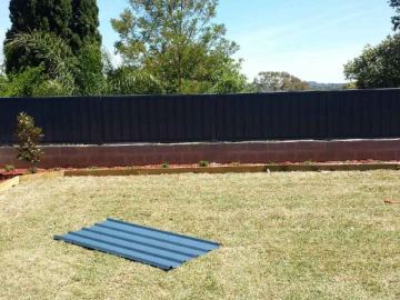 Dark Colorbond privacy fence standing on a light block garden wall across a lawn