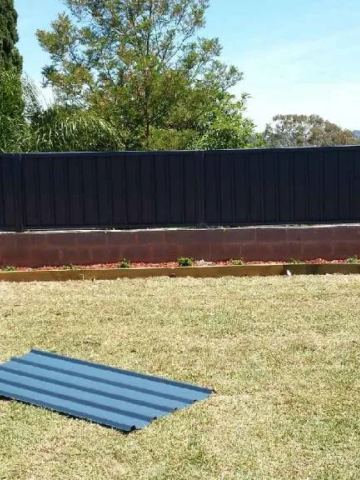 Dark Colorbond privacy fence standing on a light block garden wall across a lawn