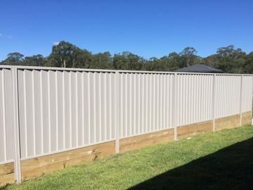 Long white Colorbond privacy fence standing on a timber plinth across a lawn