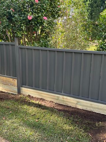 Charcoal Colorbond privacy fence sitting on a new timber sleeper retaining wall beside garden shrubs