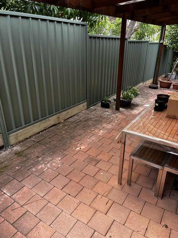 Light grey Colorbond privacy fence along a paved courtyard with a table and pot plants