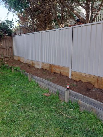 Cream Colorbond privacy fence standing on a raised timber sleeper garden bed