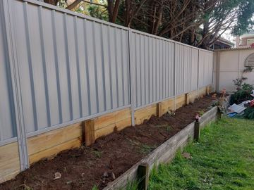 Cream Colorbond privacy fence with a newly filled timber garden bed at the base