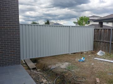 Light grey Colorbond privacy fence on a bare side yard between a house and a timber neighbour fence