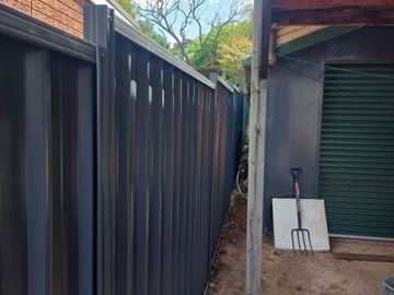 Charcoal Colorbond privacy fence running toward a matching roller door