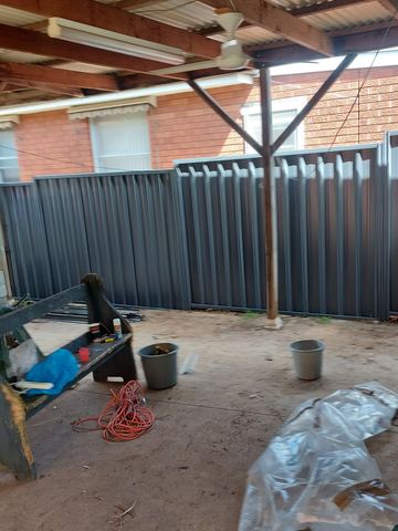 Charcoal Colorbond privacy fence across an open backyard with buckets on the dirt