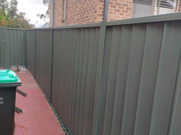 Charcoal Colorbond privacy fence following a red paved path