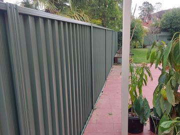 Charcoal Colorbond privacy fence along red paving with a potted plant in the foreground