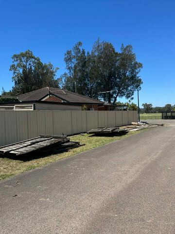 Cream Colorbond privacy fence along a sealed road with leftover boards on the grass