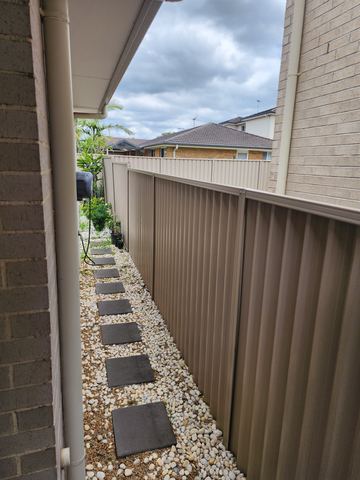 Cream Colorbond privacy fence running under the eave beside a pebble-lined path