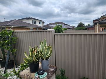 Beige Colorbond privacy fence behind potted plants on a courtyard bench