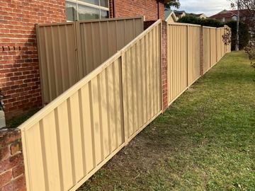 Long cream Colorbond privacy fence along a side lawn beside a brick house