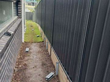 Charcoal Colorbond privacy fence along a dirt side yard beside a house wall