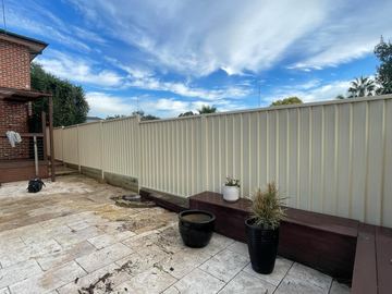 Cream Colorbond privacy fence on a paved courtyard with a bench and planter