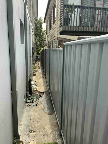 Light grey Colorbond privacy fence closing a narrow service passage beside a house