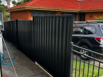 Black Colorbond privacy fence beside a parked four-wheel-drive and a steel handrail