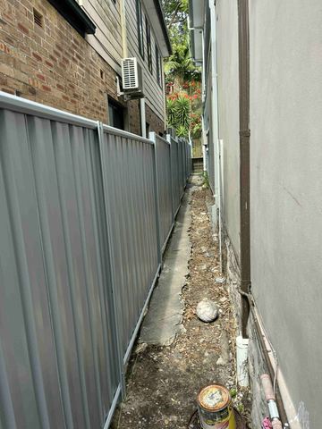 Mid grey Colorbond privacy fence forming a tight side path against a house wall