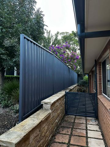 Navy Colorbond privacy fence along a house with a matching slat pedestrian gate