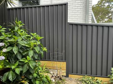 Charcoal Colorbond privacy fence sitting on a yellow-toned timber sleeper