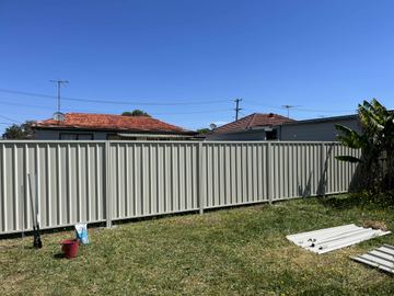 Long cream Colorbond privacy fence across an open lawn with a leftover rail