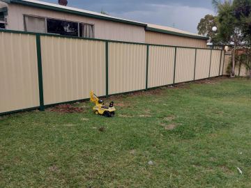 Long cream Colorbond privacy fence with green posts across a backyard lawn