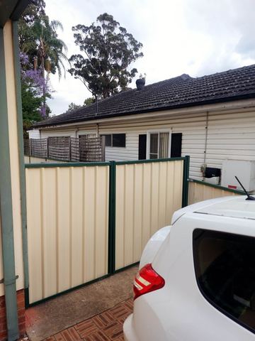 Cream Colorbond privacy fence with green posts behind a weatherboard house