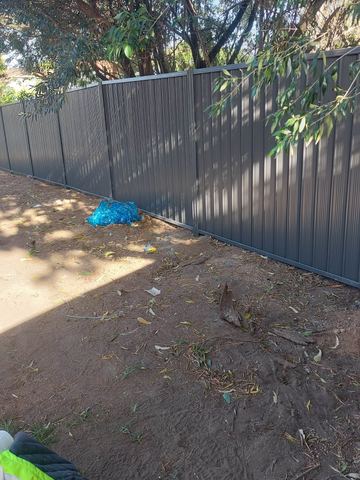 Charcoal Colorbond privacy fence across a dirt backyard with a blue bag on the ground