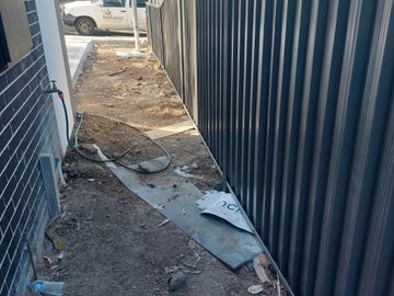 Charcoal Colorbond privacy fence along a dirt side setback beside a house