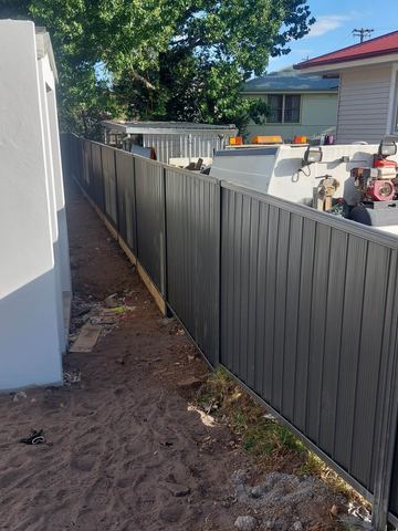 Charcoal Colorbond privacy fence running past a garden shed with tools on top