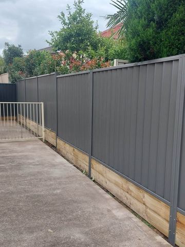 Charcoal Colorbond privacy fence on sleepers with a white garden gate in the opening