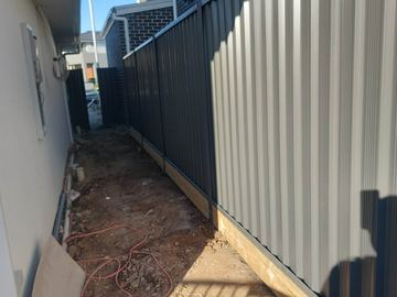 Charcoal Colorbond privacy fence in a dirt side passage beside a house