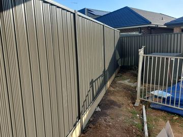 Beige Colorbond privacy fence with a white pool-mesh gate on a dirt yard