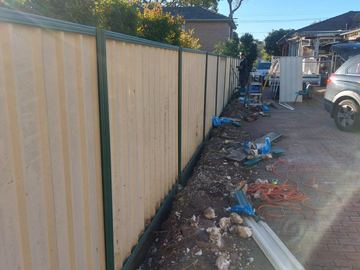 Cream Colorbond privacy fence with green posts along a building-site boundary