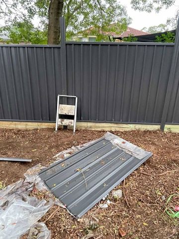Charcoal Colorbond privacy fence on a timber sleeper across a dirt yard