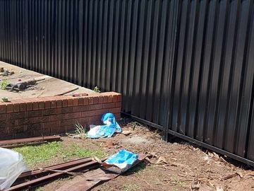 Black Colorbond privacy fence beside a low brick wall and leftover rails