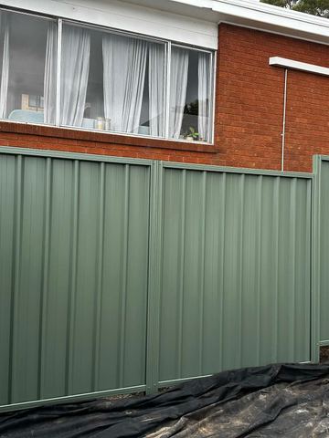 Green-grey Colorbond privacy fence in front of a two-storey brick house