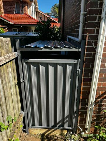 The scene shows a mid grey corrugated steel fence where sleepers form the base.