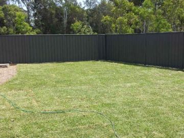 Long charcoal Colorbond privacy fence stretching across a backyard lawn