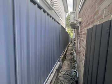 Dark Colorbond privacy fence filling a tight side passage against a brick house